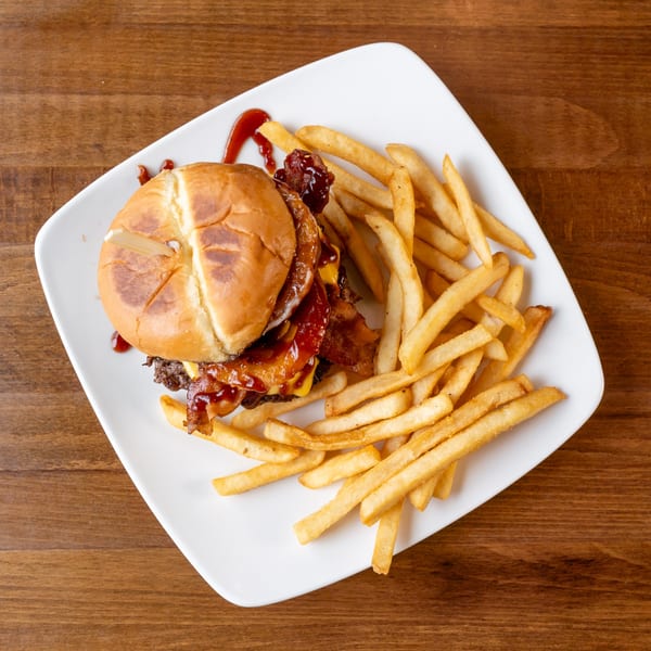 Top-down view of a bacon cheeseburger with BBQ sauce and a side of golden french fries.