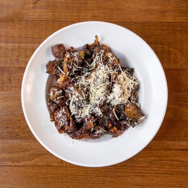 Crispy fried Brussels sprouts with grated Parmesan cheese in a white bowl on a wooden table.