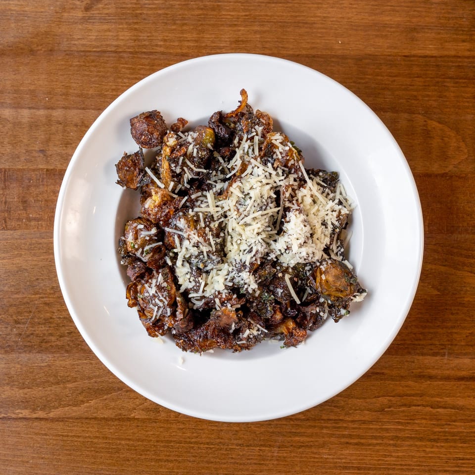 Crispy fried Brussels sprouts with grated Parmesan cheese in a white bowl on a wooden table.