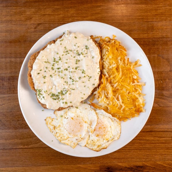 Chicken fried steak with gravy, hash browns, and two fried eggs on a white plate.