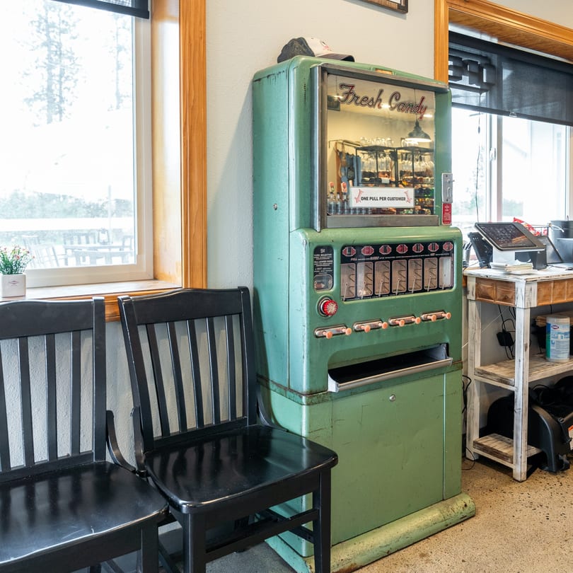 Vintage green "Fresh Candy" vending machine next to black chairs and a window.