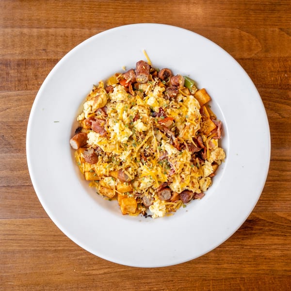 A large white bowl filled with a breakfast scramble of eggs, sausage, potatoes, and cheese.