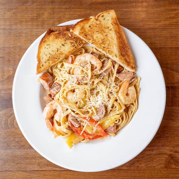 Creamy pasta with shrimp, sausage, bell peppers, and grated cheese, served with toasted bread.