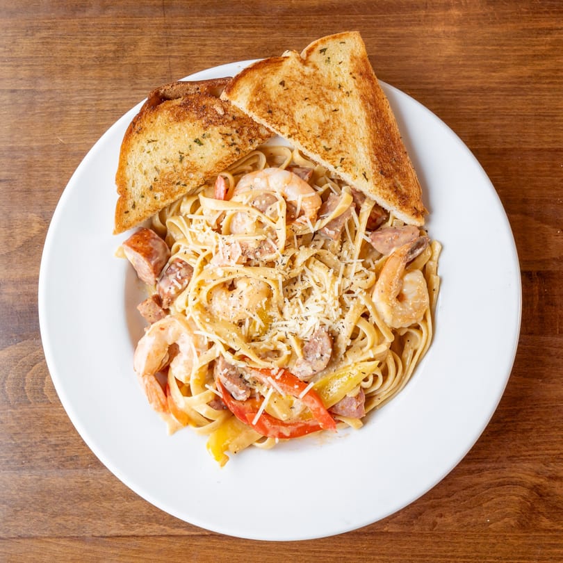 Creamy pasta with shrimp, sausage, bell peppers, and grated cheese, served with toasted bread.