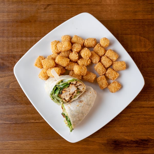 Chicken wrap with lettuce and tater tots on a white square plate on a wooden table.