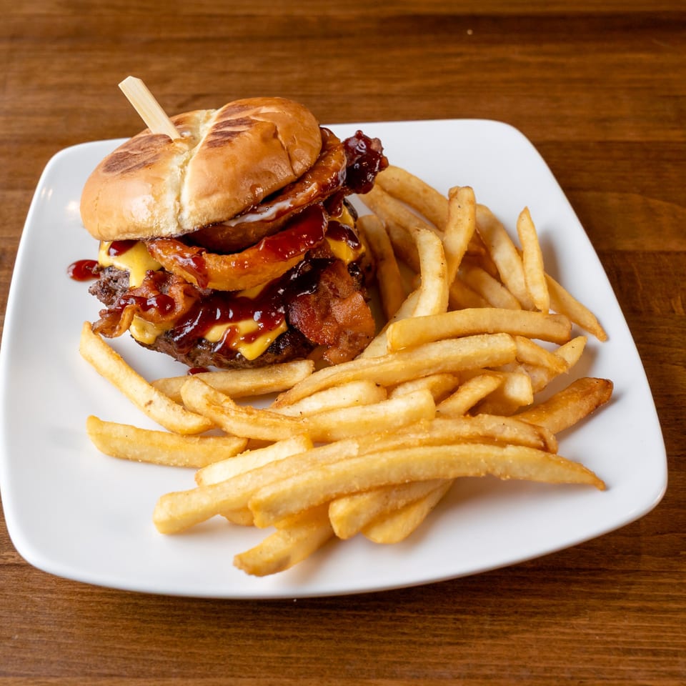 A BBQ bacon cheeseburger with onion rings and a side of golden french fries on a white plate.