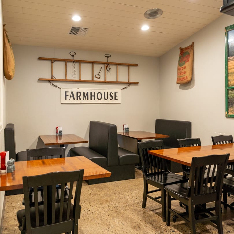 Restaurant dining room with wooden tables, black chairs, and booths, featuring a "FARMHOUSE" sign.