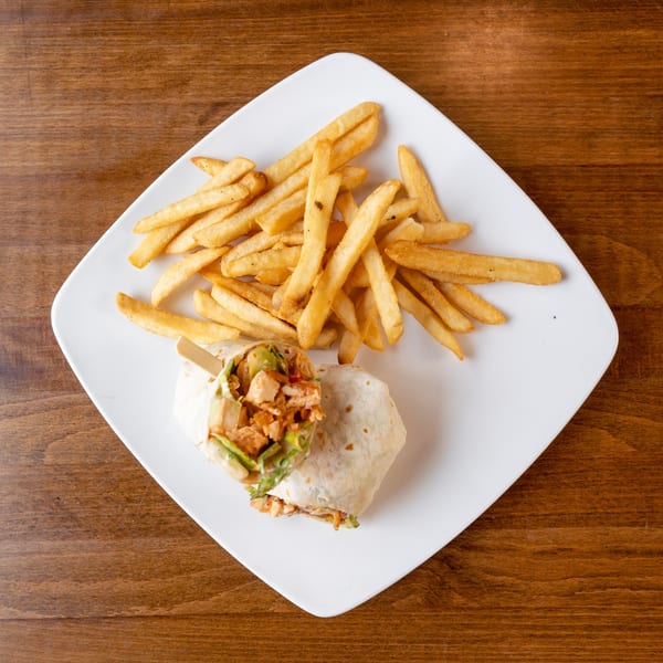 A chicken wrap with fries on a white plate, viewed from above on a wooden table.