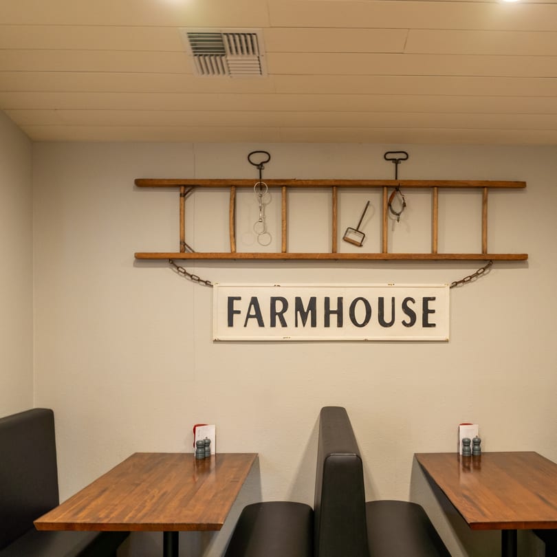 A restaurant booth with a wooden table, salt and pepper shakers, and a "FARMHOUSE" sign.